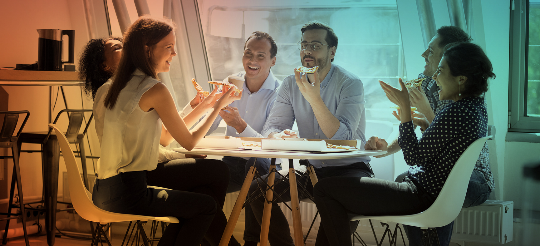 Team gathers around a table in the office to relax and share a pizza as a way to reduce stress in the office.