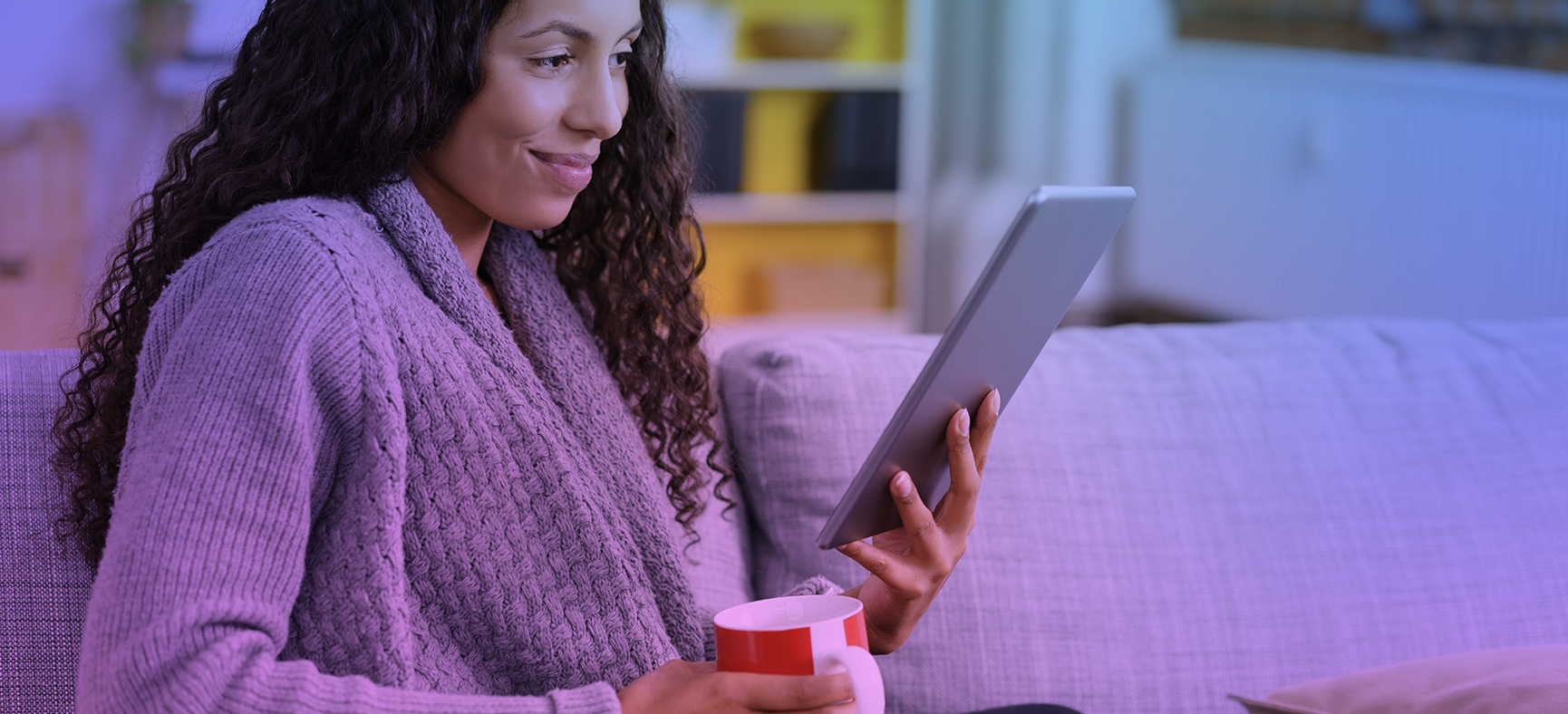 Woman reads a blog on her couch while sipping a mug of coffee