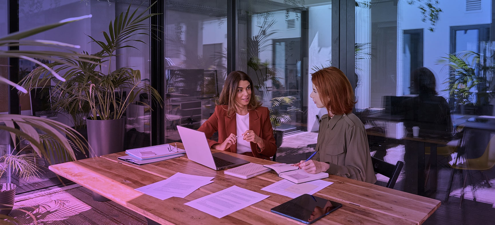 Two business women discuss compliance outsourcing at large desk